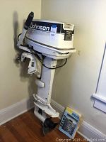 Full view of Johnson 30 HP outboard boat motor standing on wooden floor near wall, showing side profile with motor propeller and cable.