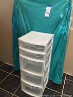 Sterilite white plastic storage organizer with four drawers, placed in front of a teal fabric backdrop.