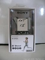 Front view of Sony WI-SP500 Bluetooth wireless sports headset in retail packaging. White earbuds and neckband visible. Packaging shows model WI-SP500 and sports usage illustration.