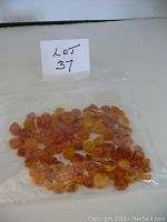 Plastic bag containing an assortment of small amber beads, visible through the bag; several colors and shapes including round and irregular, all predrilled.