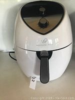 Front view of white Wolfgang Puck air fryer showing top control dials and front basket handle.