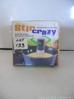 Box of Stir Crazy Automatic Hands-Free Sauce Stirrer showing front panel, branding and product photograph of the device in use stirring food in a pot.