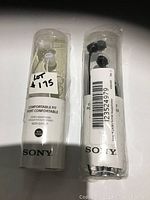 Two Sony MDR-EX15LP stereo earbud headphones in original clear plastic packaging, one white and one black.