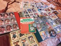 Photo showing multiple loose baseball and hockey cards spread out on a surface, with several binders of plastic sleeves containing more cards, a boxed set of Baseball's All-Time Greats cards, and coin-like collectibles.