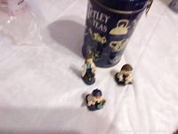 Photo of blue Tetley Tea metal can with gold detailing and three small ceramic figures on white surface