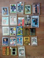 Photo of 24 sports cards arranged on a flat surface, mostly hockey cards with two baseball cards. Some cards are in sleeves or hard cases, some show rookie status, some show autographs.