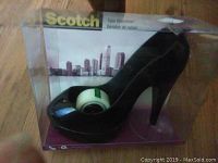 Photo of the Scotch tape dispenser in black high heel shoe design inside clear plastic packaging displaying product and tape roll.