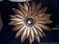 Front view of sunflower wall mirror showing multiple layers of textured gold petals and central circular mirror reflecting surroundings.
