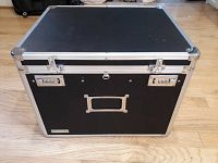 Closed black Vaultz file chest with metal reinforced edges, two combination locks, label holder, and handle on front, sitting on wooden floor.