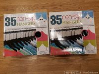 Two unopened boxes of 35 black non-slip hangers each, arranged side by side on a wooden floor.