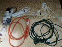 Top view showing 7 power cords of various types: white and beige power strips with multiple outlets and on/off switches, orange and green extension cords.