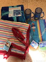 Photo showing all items in the lot: large beach towel, two freezer mugs, picnic blanket, vinyl tablecloth, two sets of coasters
