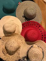 Top view of six assorted large brim summer hats, displaying a variety of colors and weaving styles.