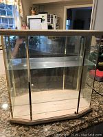 Front view of the wood display cabinet with glass sides, front, and one glass shelf inside on a wood base.