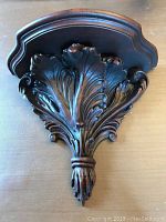 Front view of the resin faux carved wood wall shelf sconce showing intricate leaf design and brown wooden top.