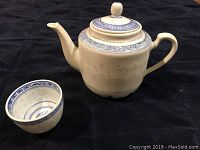 Side view of cream-colored ceramic teapot with blue floral geometric designs and matching teacup
