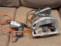 Photo showing vintage corded drill and heavy duty circular saw on a couch, focused on drill with orange power cord visible.