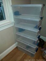Stacked view of six rectangular clear plastic DVD storage boxes with lids showing blue locking tabs, one lock missing on one box.