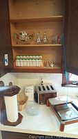 Full kitchen cabinet view showing milk glass spice jars on shelf, glassware items, toaster, and other kitchen items on counter.