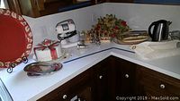 Wide view of kitchen counter with all referenced items arranged for display, including mixer, cake keeper, tea kettle, serving trays, rose garlands, and more.