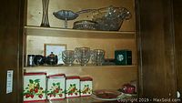 Shelf with vintage metal canisters with cherry design, assorted cut glass mugs, glass punch mugs, and small metal teapot