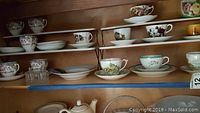 Shelves filled with various porcelain tea cups and saucers with floral and bird designs, some with gold accents.