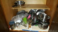 Cupboard shelves with assorted pots, pans, strainers, and food prep items stacked together