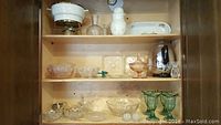 Shelf with a variety of glassware including cut crystal bowls, depression glass plates, two green glass sundae goblets, small serving dishes, salt dips, and an electric percolator.