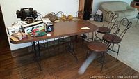 Photo showing rectangular dining table with faux woodgrain laminate top, black wrought iron base, surrounded by six wrought iron chairs with vinyl seats. Contents on table not included.
