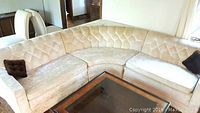 Full view of the cream-colored velour sectional sofa showing the three connected pieces with two brown accent pillows.