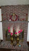 Two brass urn-style vases with pink faux flowers and white dried twigs, displayed on hearth in front of brick fireplace.