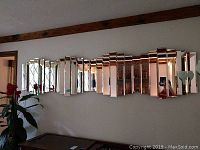 Photo of one mirrored wall decor piece mounted on a white wall, showing the segmented mirrors reflecting room details.