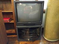 Front view of the Mitsubishi CRT TV with the cabinet doors open, revealing storage space inside the cabinet underneath the TV.