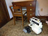Photo of wooden sewing machine cabinet with power cords and plugged-in Singer sewing machine beside a wooden chair