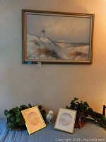 Two framed John Cheng limited edition prints placed on rattan trays on a table with faux owl figurine among plants.