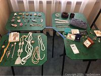 Overview of the entire lot displayed on four green tables showing a variety of costume jewelry pieces including watches, necklaces, bracelets, and boxed smaller items.
