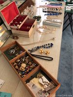 Photo showing numerous necklaces, earrings, and bracelets spread out on a table and partially in an open jewelry box and wooden drawer units.