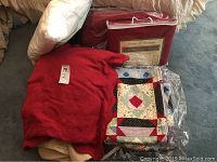 Assorted pillows, quilts, bed covers and blankets including unopened red bed covers, a colorful patchwork quilt, and a red textured quilt.