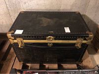 Front view of large black Overland trunk showing brass latches and lock area with visible wear and scratches