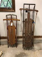 Two vintage wooden sleds side by side showing overall condition and structure.