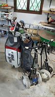 View of two golf bags filled with multiple golf clubs and one golf push caddy