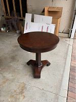 Full view of round dark wood pedestal side table showing tabletop and base in a garage setting.