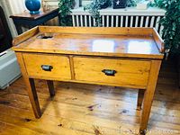Front view of antique pine desk with two drawers and ornate metal pulls, showing inkwell hole on top surface.