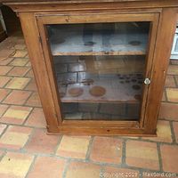 Front view of the antique display cabinet showing single glass door and two shelves with circular stains.