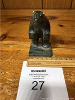 Front view of dark stone standing bear sculpture showing signature and scale ruler indicating height.