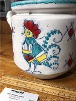 Close-up of the colorful hand-painted rooster on the pot's side with ruler for scale.