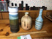 Three vintage pottery vases on wooden surface with ruler for scale.