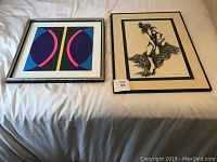 Two framed paintings side by side on a bed; left is abstract geometric art, right is black and white figurative drawing.