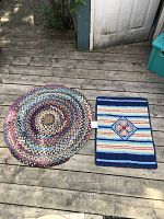 Photo showing both small hand knotted wool carpets: circular multicolor braided rug and rectangular striped and floral pattern rug.