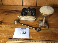 All three items on wooden surface: brass pin cushion, brass candle snuffer, Wega opera mini binoculars in case